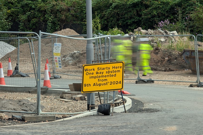 Roadworks sign with construction workers in the background.